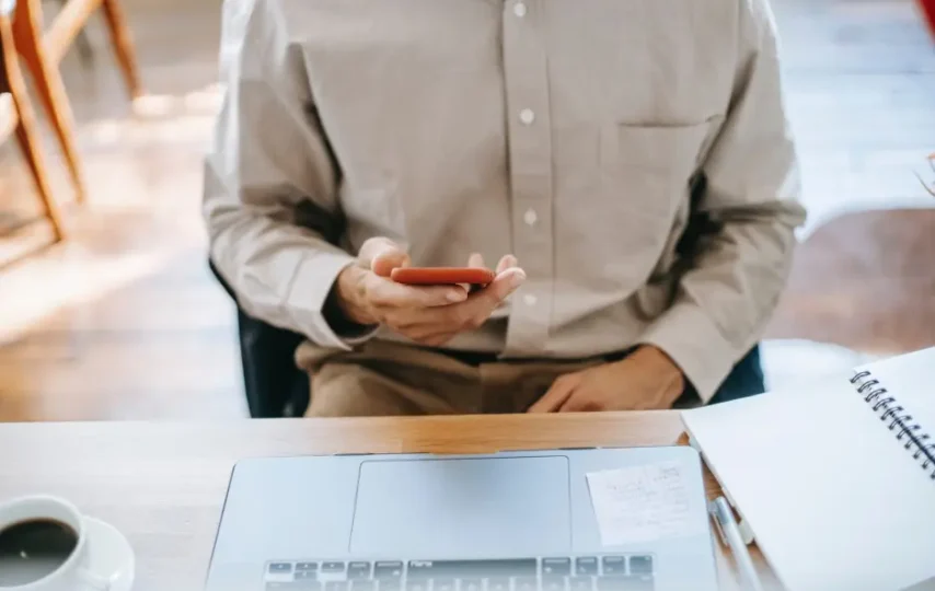 کار مرد با موبایل جلوی لپتاپ