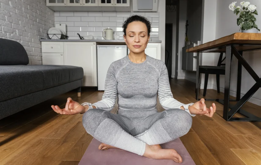 یوگا زن نشسته با لباس اسپرت خاکستری در وسط خانه
