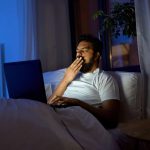 خمیازه مرد در تخت پشت لپتاپ